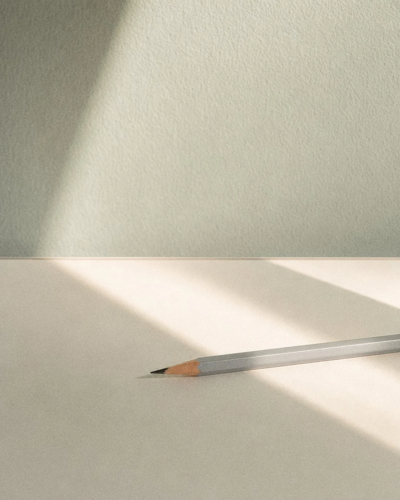 Ein hellgrauer Bleistift liegt schräg auf einer weißen Fläche im Sonnenlicht, mit KI erzeugt