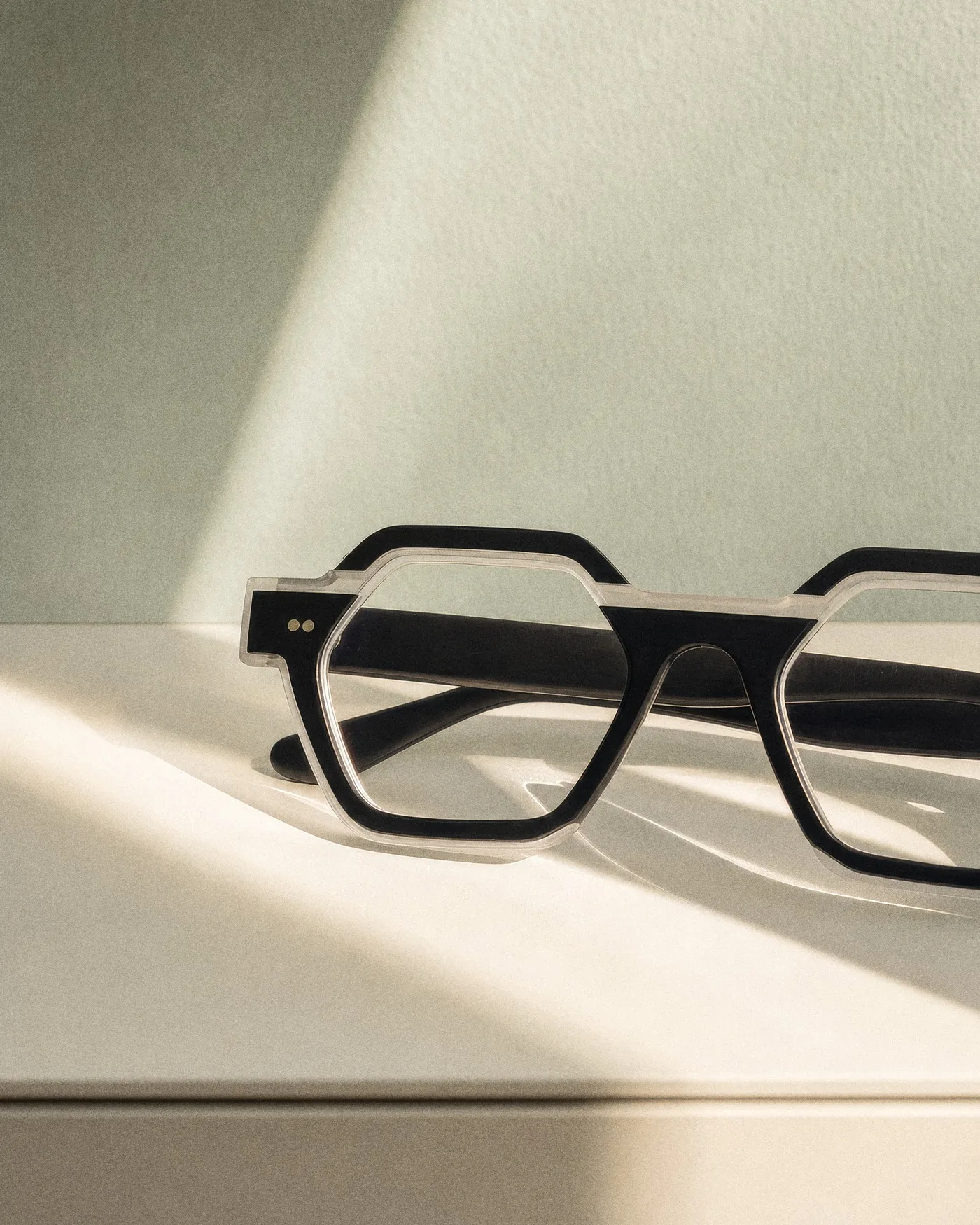 Eine eckige schwarze Brille, zusammengeklappt auf einer weißen Fläche im Sonnenlicht, mit KI erzeugt