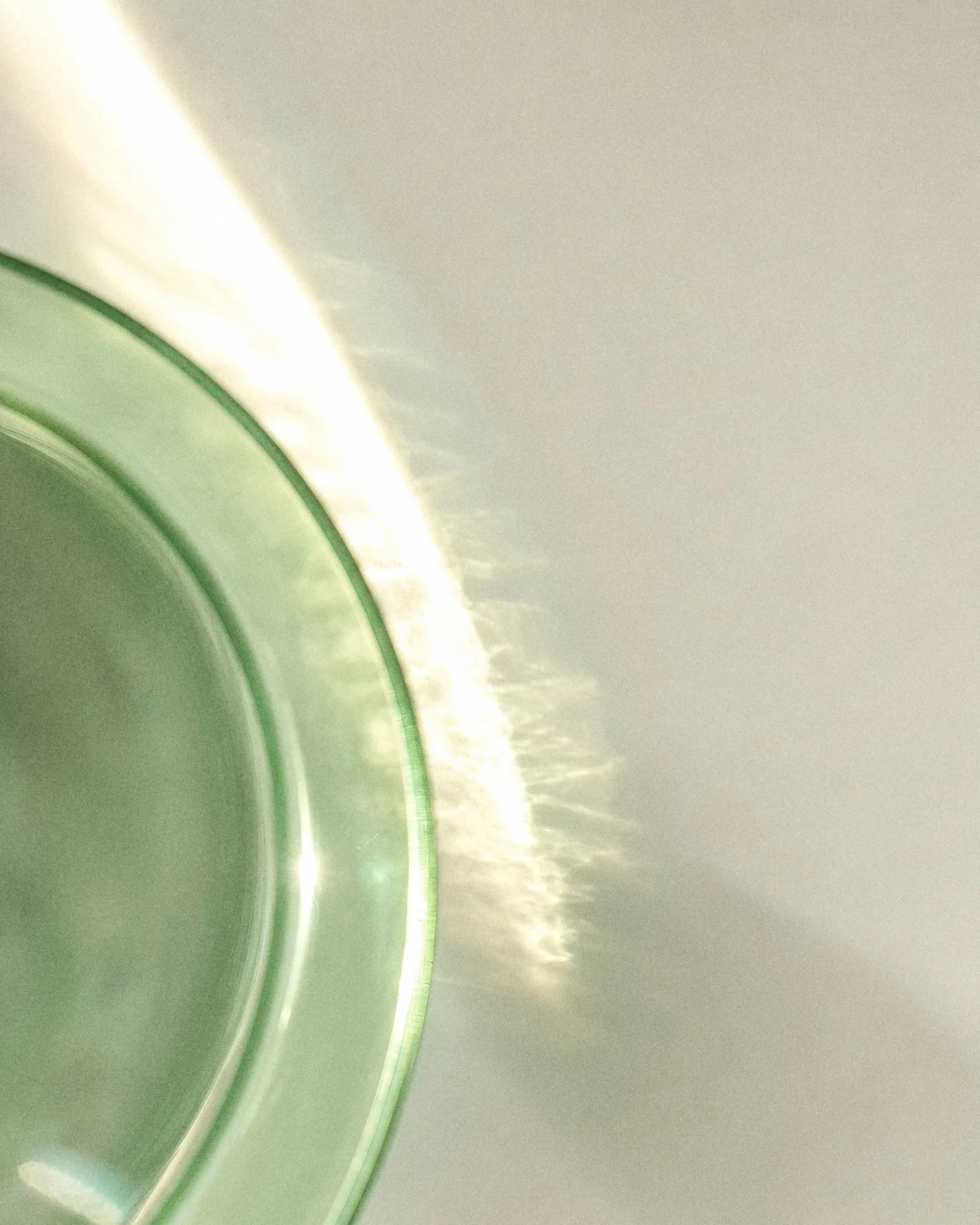 Der Rand eines grünen Glases mit Wasser, durch das ein Streifen Sonnenlicht fällt, mit KI erzeugt