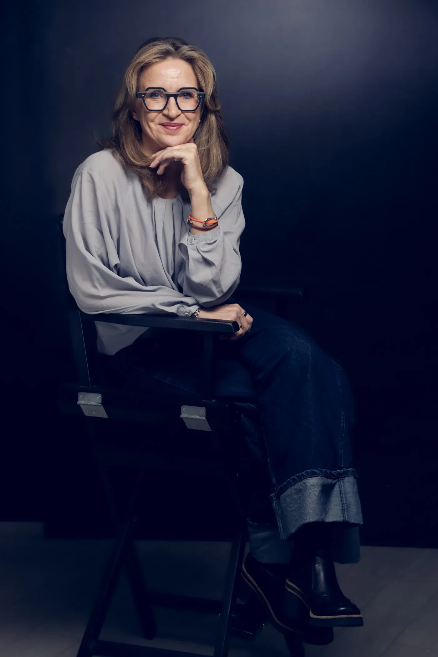 Katrin Funke, sitzend vor dunklem Grund, mit Brille, die Hand am Kinn