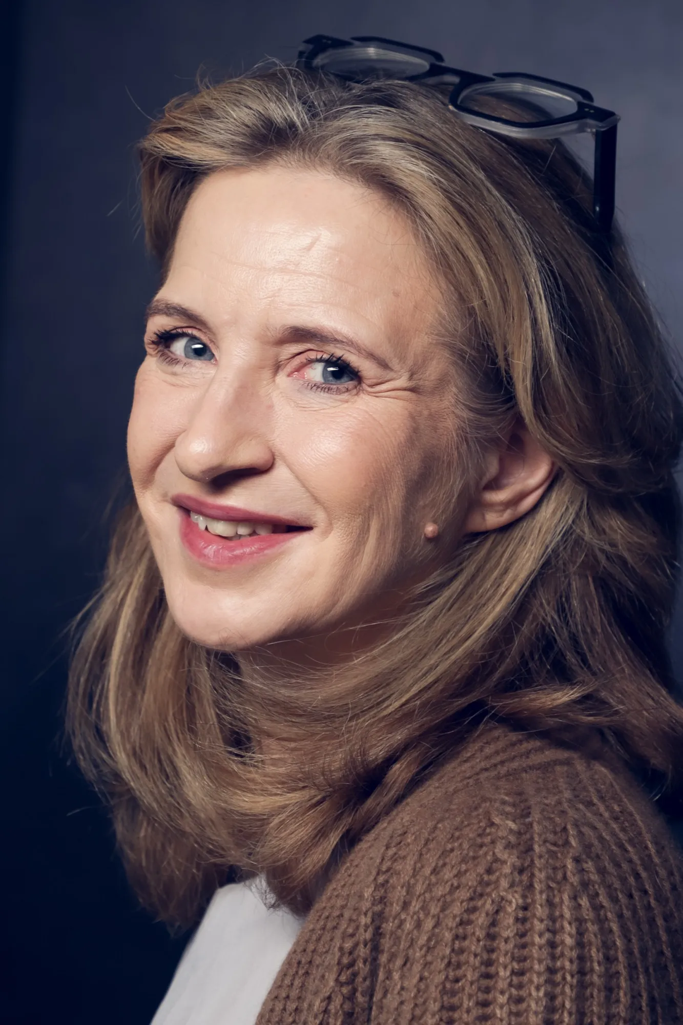 Katrin Funke, Porträt: Blick über die Schulter, lächelnd, Brille im Haar, brauner Strickpullover